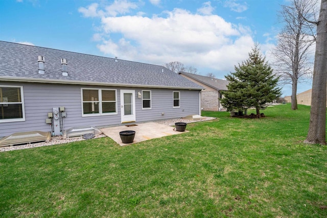 back of house featuring a lawn, a shingled roof, and a patio area