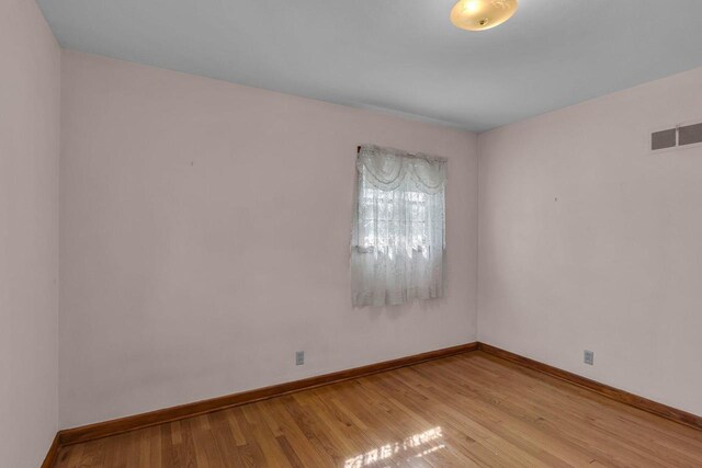 empty room with visible vents, light wood-style flooring, and baseboards