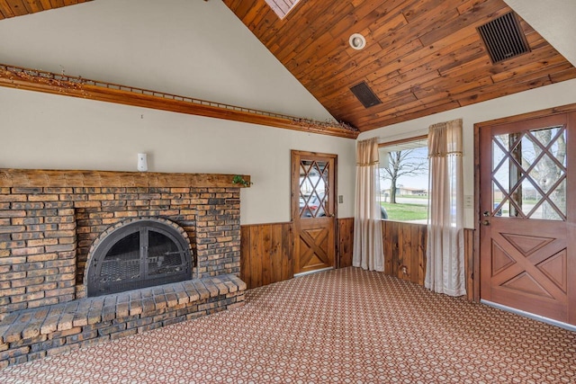 unfurnished living room with wainscoting, wood walls, a brick fireplace, high vaulted ceiling, and carpet