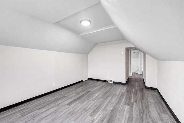 bonus room featuring baseboards, lofted ceiling, wood finished floors, and visible vents