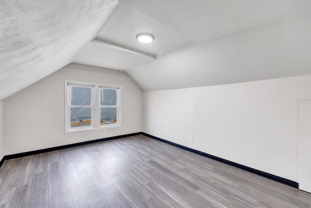 additional living space featuring baseboards, wood finished floors, and lofted ceiling