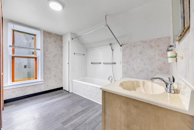 bathroom with vanity, wood finished floors, baseboards, wallpapered walls, and shower / washtub combination