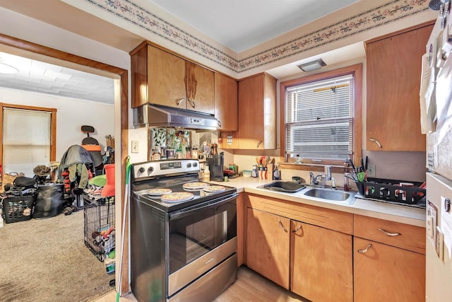 kitchen with a sink, light countertops, electric stove, under cabinet range hood, and a wealth of natural light