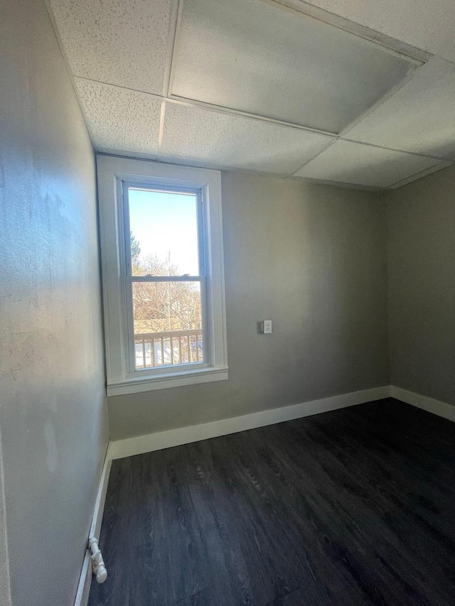 empty room featuring baseboards, dark wood-type flooring, and a paneled ceiling