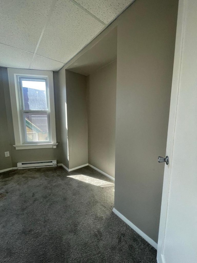 spare room featuring baseboards, a paneled ceiling, dark carpet, and a baseboard radiator