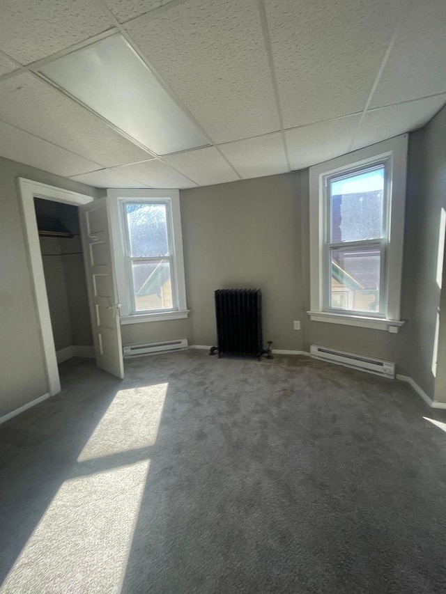 unfurnished bedroom with radiator, carpet, a baseboard heating unit, and a paneled ceiling