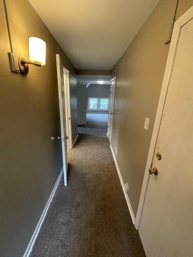 hall with baseboards and dark carpet