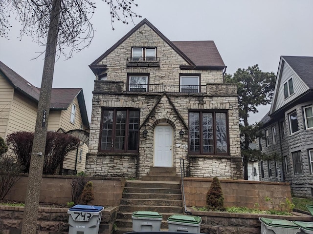 view of front of home featuring entry steps, fence, a balcony, and stone siding