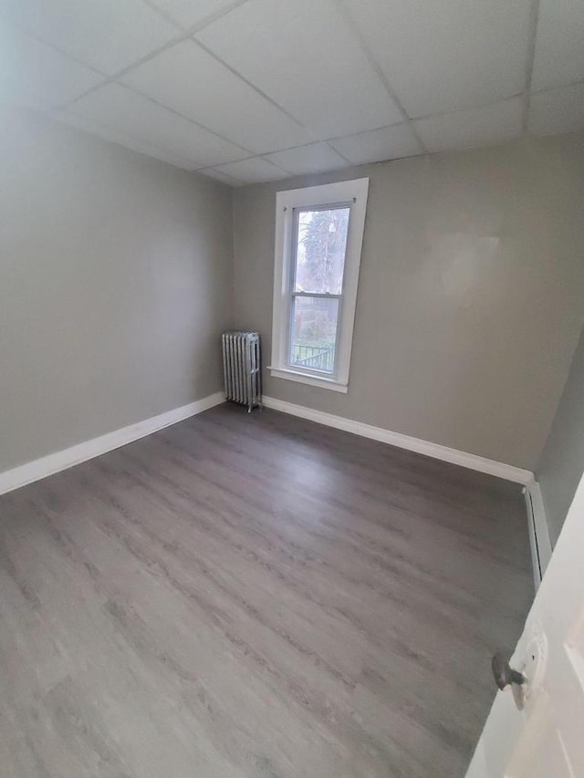 unfurnished room with baseboards, a paneled ceiling, radiator, and wood finished floors