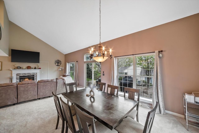 dining room with a lit fireplace, light colored carpet, high vaulted ceiling, baseboards, and a chandelier