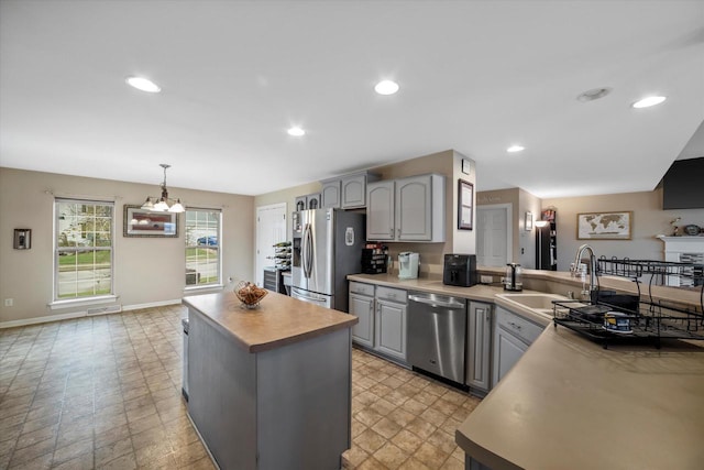 kitchen featuring a sink, a center island, stainless steel appliances, baseboards, and gray cabinetry