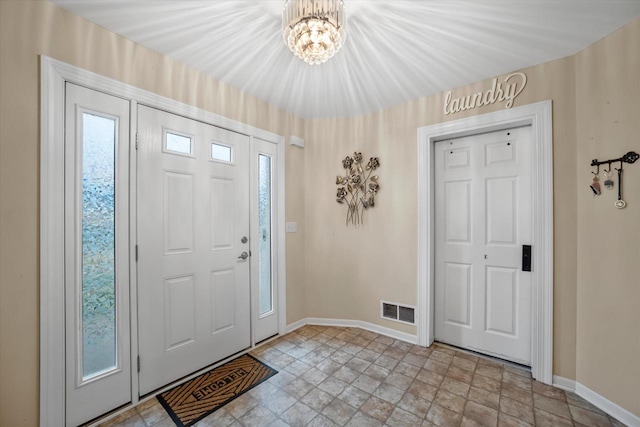 entrance foyer with baseboards, stone finish floor, a notable chandelier, and visible vents
