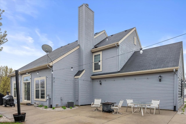 back of house with a patio, roof with shingles, a chimney, and cooling unit