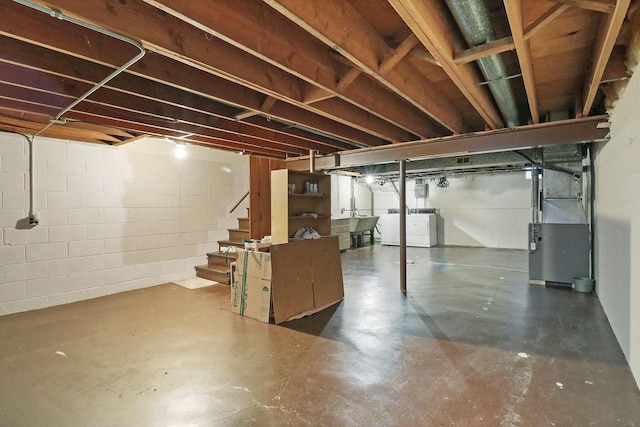unfinished below grade area with heating unit, stairs, separate washer and dryer, a sink, and concrete block wall