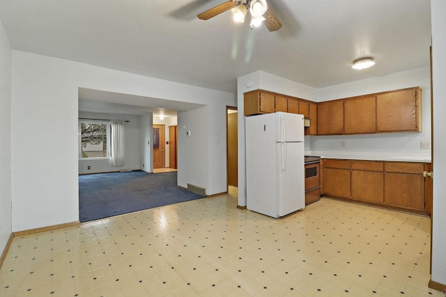 kitchen with brown cabinetry, a ceiling fan, stainless steel range with electric cooktop, light countertops, and freestanding refrigerator
