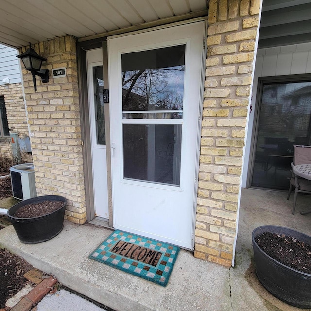 doorway to property featuring brick siding and cooling unit