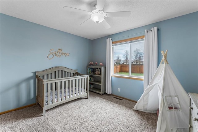 bedroom featuring carpet flooring, a nursery area, a textured ceiling, a ceiling fan, and baseboards