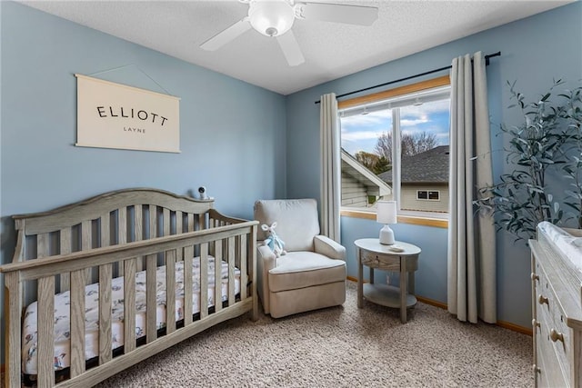 carpeted bedroom with baseboards, a textured ceiling, a crib, and ceiling fan