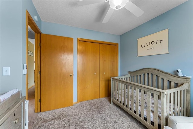 carpeted bedroom with a crib, a ceiling fan, and a closet