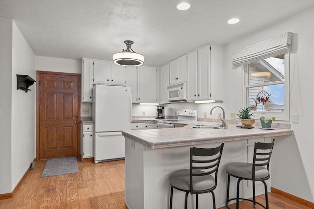 kitchen featuring white appliances, a peninsula, white cabinets, and a sink
