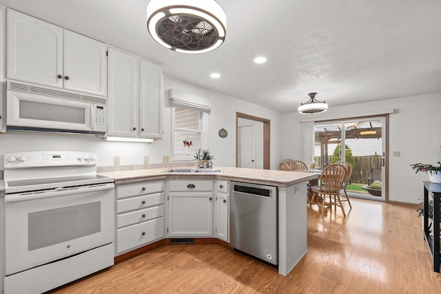 kitchen featuring a sink, a peninsula, white cabinets, and white appliances