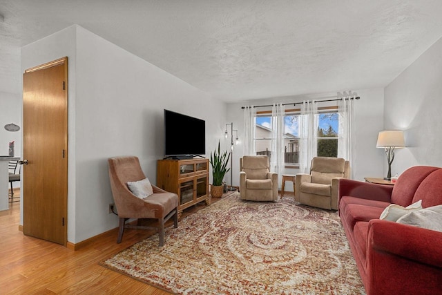 living area featuring a textured ceiling, baseboards, and light wood finished floors