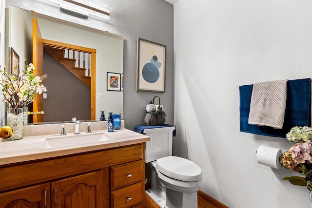 bathroom featuring vanity, a textured wall, toilet, and wood finished floors