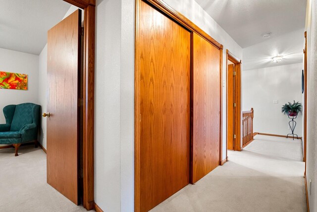 hallway with baseboards, carpet, and an upstairs landing