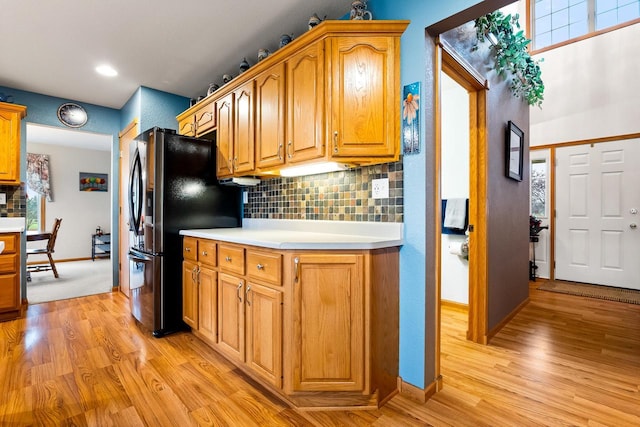 kitchen featuring light wood-style floors, decorative backsplash, light countertops, baseboards, and stainless steel fridge