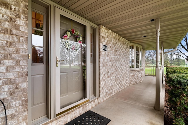 doorway to property with a porch and brick siding