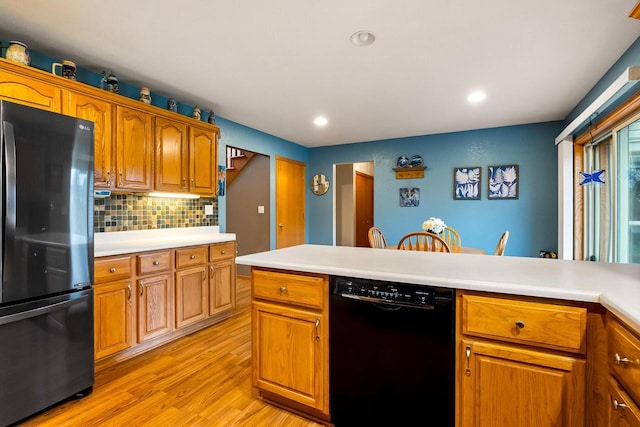 kitchen with backsplash, brown cabinets, light countertops, black appliances, and light wood-style flooring