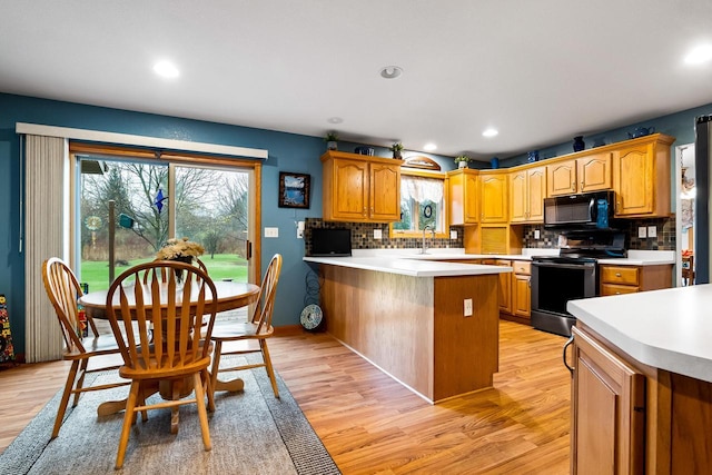 kitchen featuring decorative backsplash, black microwave, light countertops, light wood finished floors, and electric stove