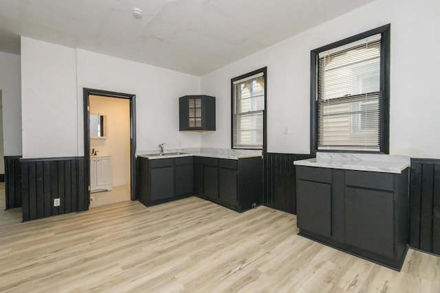 kitchen with dark cabinetry, wainscoting, a sink, and light wood-type flooring
