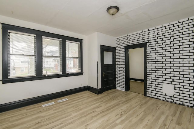empty room featuring baseboards, light wood-type flooring, brick wall, and visible vents