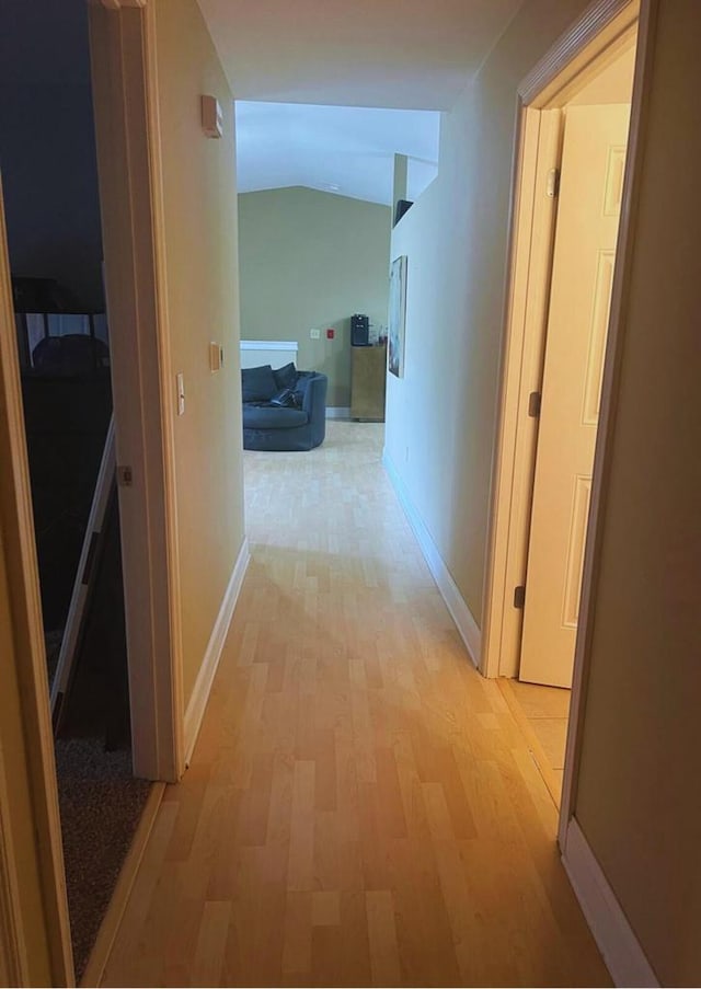 hall with baseboards, vaulted ceiling, and light wood-style flooring