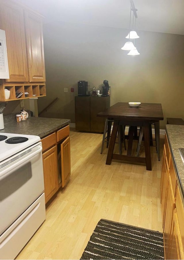 kitchen with brown cabinets, dark countertops, white appliances, light wood-type flooring, and pendant lighting