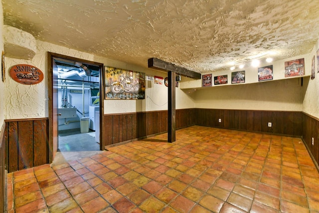 finished below grade area featuring a wainscoted wall, wood walls, and a textured ceiling