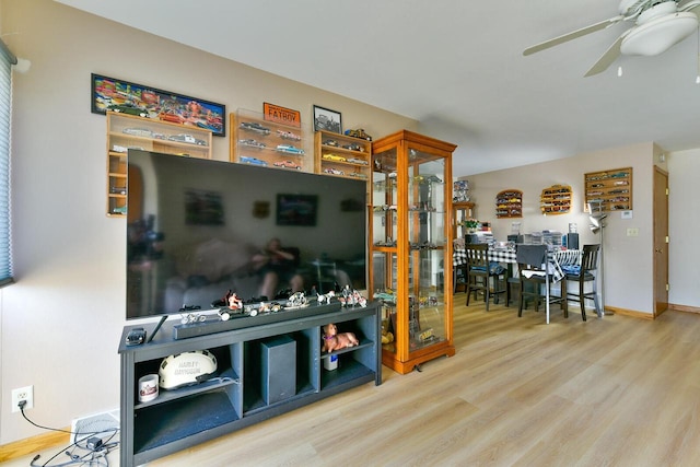 living area featuring baseboards, a ceiling fan, and wood finished floors