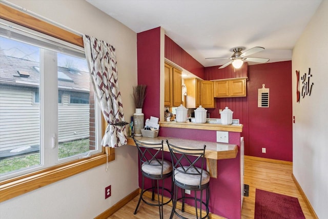 kitchen featuring ceiling fan, a kitchen breakfast bar, baseboards, a peninsula, and light wood-style flooring