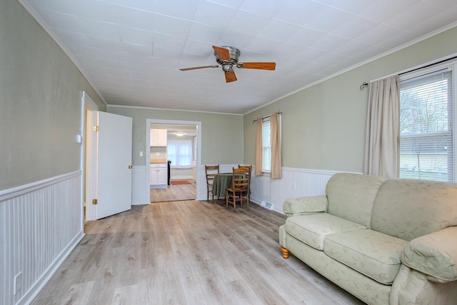 living room with light wood-style floors, crown molding, wainscoting, and ceiling fan