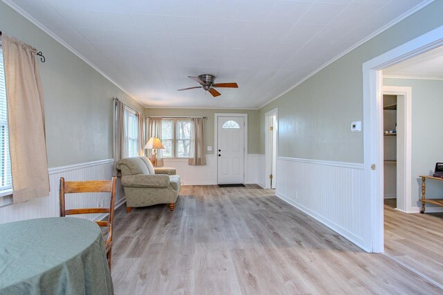 foyer entrance with crown molding, a wainscoted wall, ceiling fan, and wood finished floors