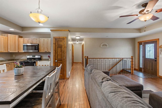 kitchen with light brown cabinetry, baseboards, open floor plan, light wood-type flooring, and appliances with stainless steel finishes