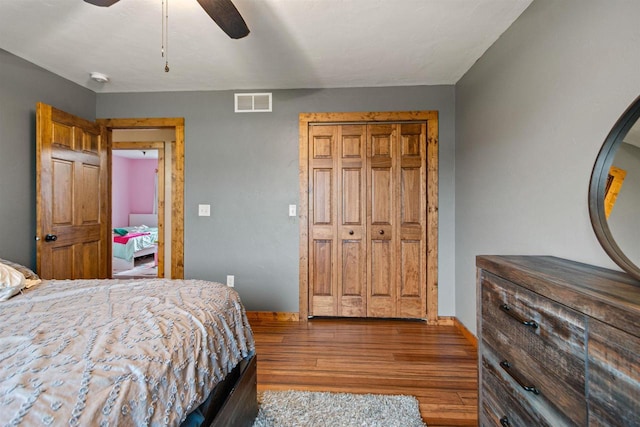 bedroom with a ceiling fan, visible vents, wood finished floors, baseboards, and a closet