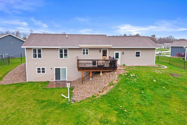 rear view of property featuring fence, roof with shingles, a yard, and a deck
