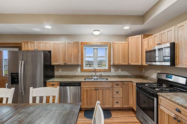 kitchen featuring appliances with stainless steel finishes, light brown cabinetry, light wood-type flooring, a sink, and stone counters