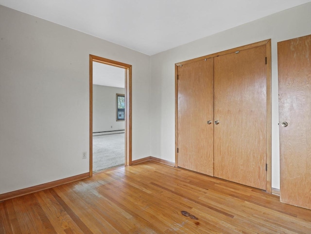 unfurnished bedroom with a closet, baseboards, a baseboard heating unit, and light wood finished floors