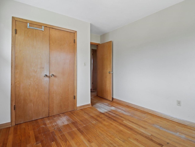 unfurnished bedroom featuring a closet, light wood-style flooring, and baseboards