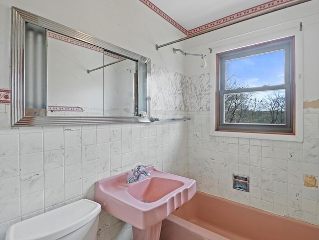 full bath with a sink, tile walls, washtub / shower combination, and toilet