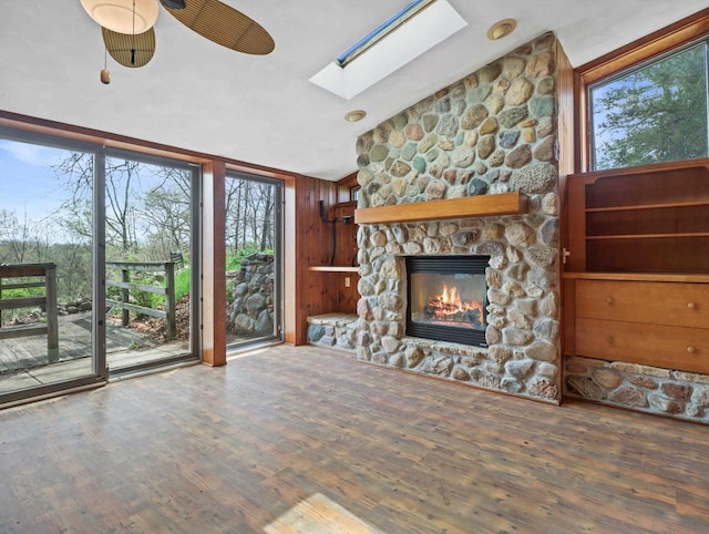 unfurnished living room featuring vaulted ceiling with skylight, ceiling fan, a stone fireplace, and wood finished floors