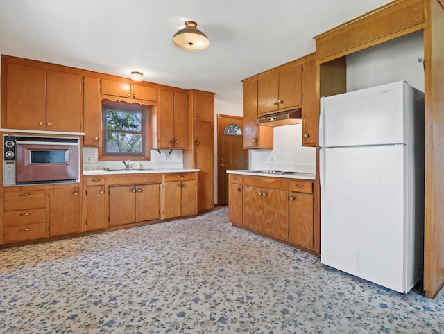 kitchen featuring brown cabinets, a sink, white appliances, light countertops, and under cabinet range hood